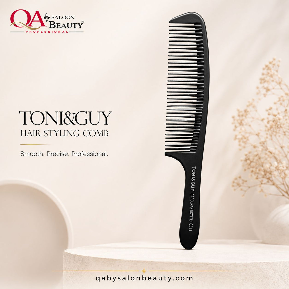 A black plastic hair styling comb by TONI&GUY stands upright on a light beige pedestal. The background is a soft cream studio setting with decorative dried flowers in a vase and branding text for QA by SALOON BEAUTY and TONI&GUY HAIR STYLING COMB.